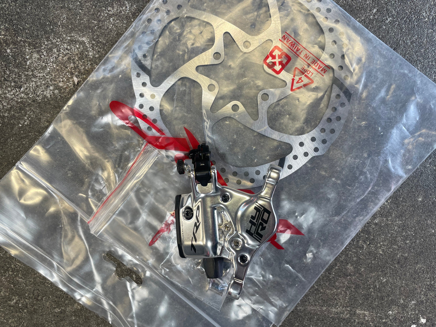 Disc brake assembly on a clear plastic bag with visible branding on a dark surface.