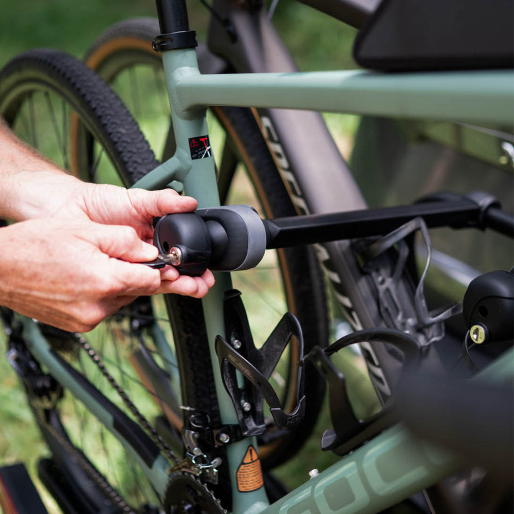 Person securing a bike lock on a bicycle with a blurred natural background