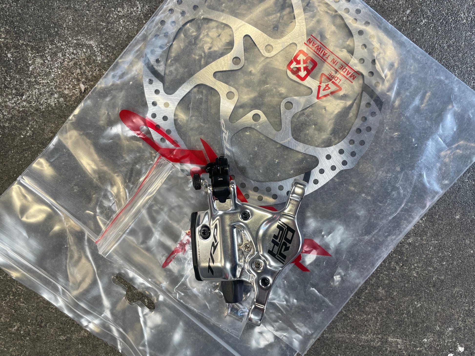 Disc brake assembly on a clear plastic bag with visible branding on a dark surface.