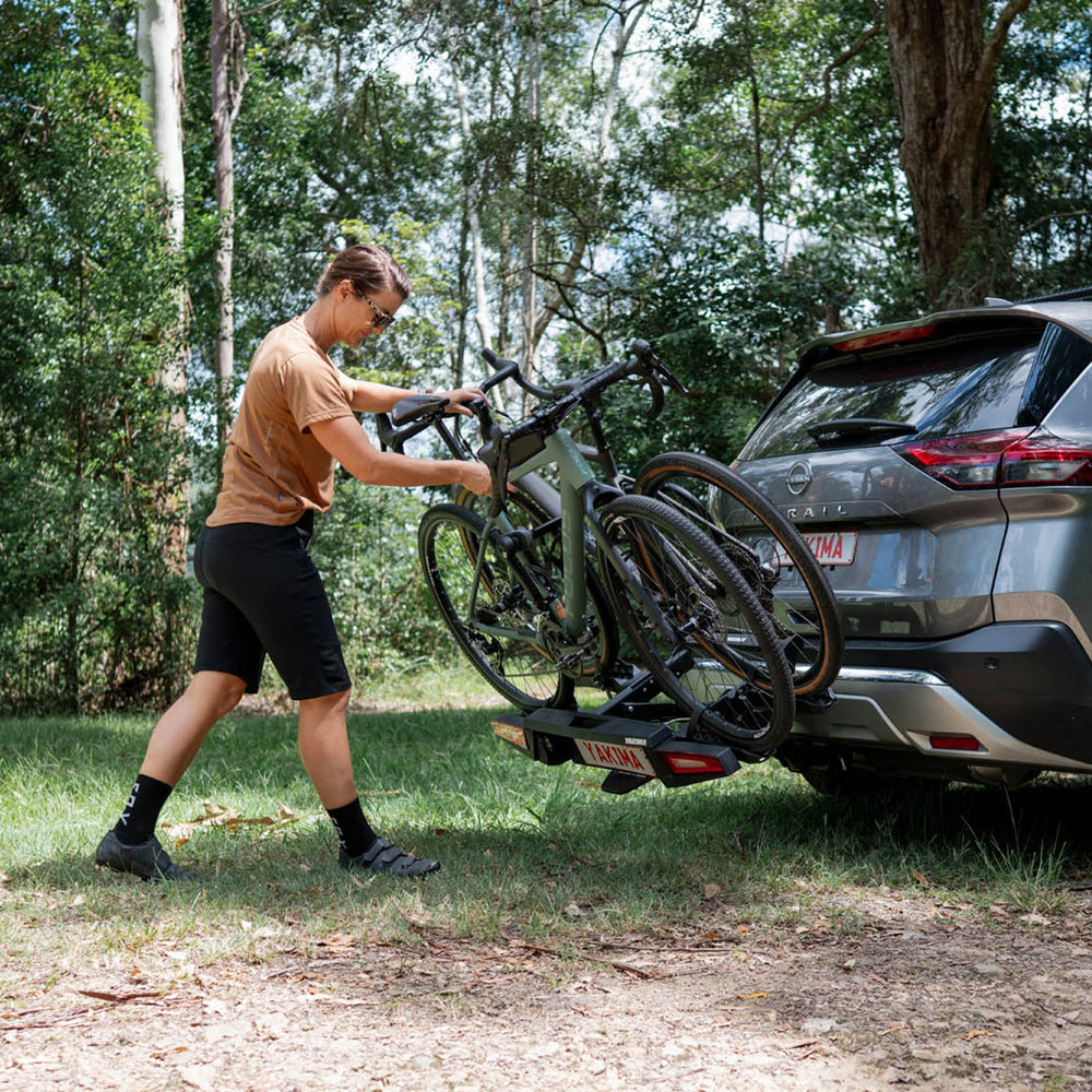Person loading a bicycle onto a car with a bike rack in a forest setting